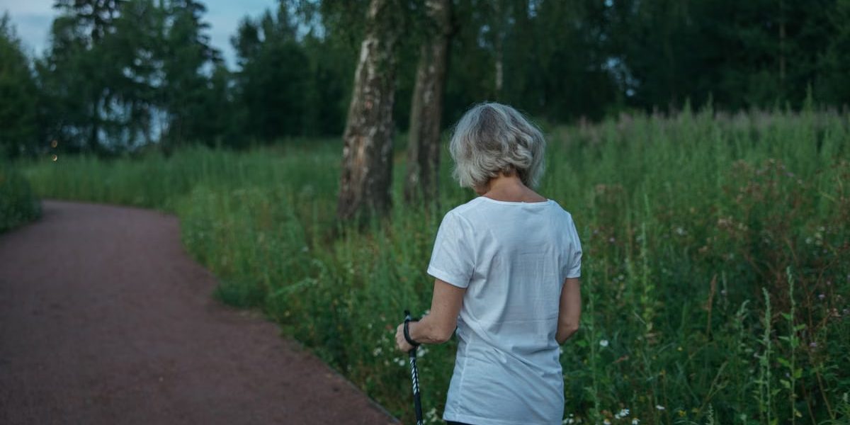 Elderly woman practicing Nordic walking on a park trail, promoting health and fitness.