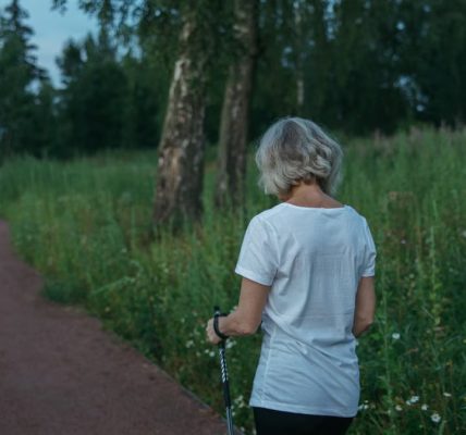 Elderly woman practicing Nordic walking on a park trail, promoting health and fitness.